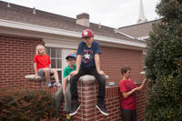 A pre-teen boy and his cousins play on a brick fence outside a Mormon LDS church at a family gathering. Tyler, Texas