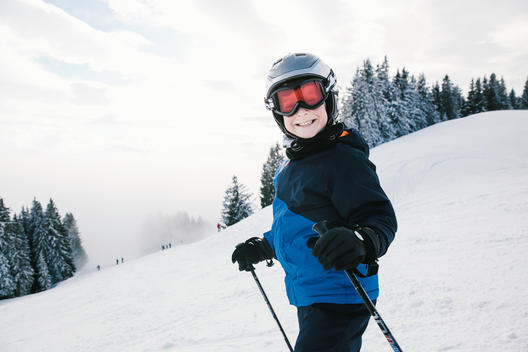 A young happy skier boy, wearing ski helmet and ski goggles, smiling to camera on a ski slope in the Tirol region in Austria.