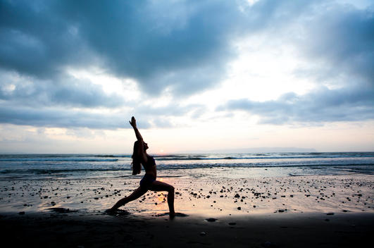 One female yoga practitioner in a warrior one pose on the beach at sunrise