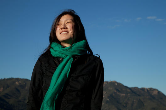 Young Asian Woman Looking Into Distance With Blue Sky And Hills In Background