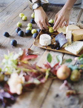 A woman at a domestic kitchen table. Arranging fresh fruit, black and green figs on a cheese board. Organic food. From farm to plate.
