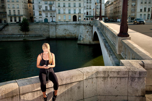 Woman in exercise clothes, sitting while using mobile phone on Seine River