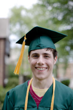 A High School Senior, Dressed In His Graduation Cap And Gown, Poses For A Portrait In His Backyard.