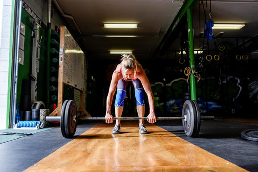 A female Crossfit athlete prepares to do the clean and jerk with barbell weights at a Crossfit gym.