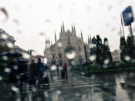 From a taxi one takes a mobile picture of a rain drenched scene with the Duomo Cathedral in Milan Italy.