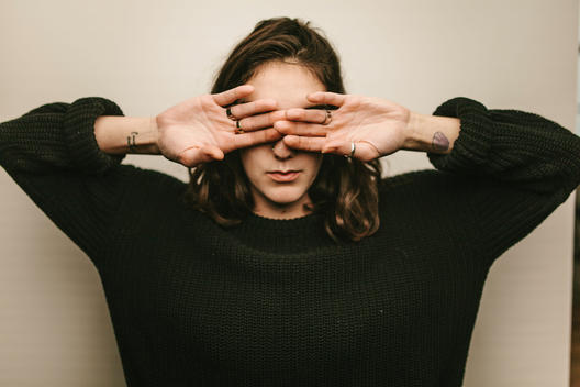 Portrait of young woman covering her eyes with hands.