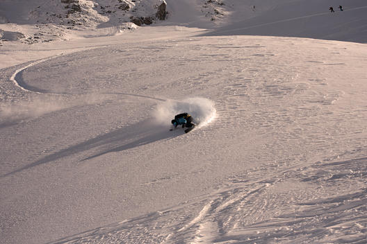 A snowboarder makes a fast and deep turn in powder Snow in the late afternoon sunlight