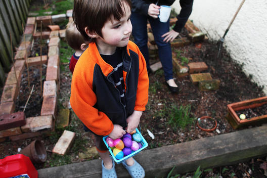 Little boy holding a basket full of Easter eggs pauses during an Easter egg hunt