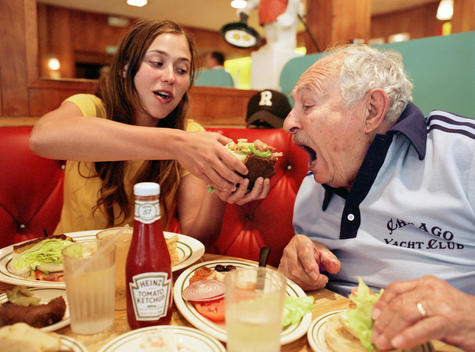Young Girl Feeds Her Much Older Boyfriend A Bite Of Her Sandwich At A Diner During Lunch.