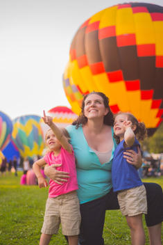 Mid adult woman and two daughters looking up and pointing at hot air balloons at festival