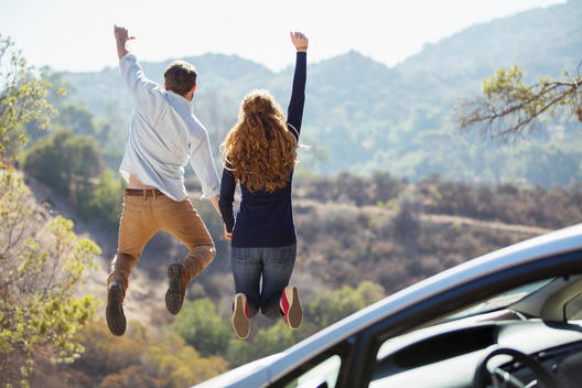 Enthusiastic couple jumping for joy outside car