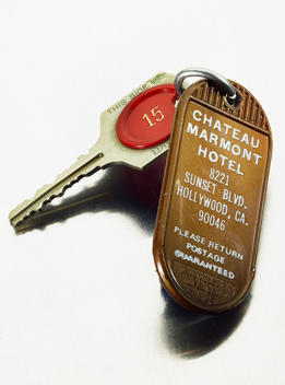 Brown plastic hotel key fob and key with red room number on white metal surface