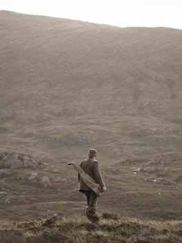 Gamekeeper standing in on a hillside with shotgun pouch over his shoulder.