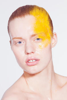 beauty image of model in studio, with vaseline clean skin, hair back and yellow colored makeup dusted on side of the face