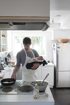 Chef Daniel Patterson holding his baby while cooking in his kitchen