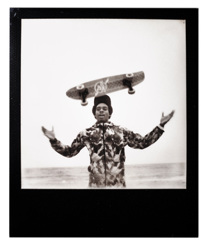 A polaroid of a young man throwing a skateboard.