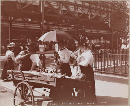 The Corner Of 6Th Avenue And 20Th Street Shows A Street Vendor Selling Fruit From A Pushcart. Behind The Vendor, The Elevated Tracks Of The 6Th Avenue Elevated Subway Can Be Seen, Also Pedestrian Traffic On 6Th Avenue.