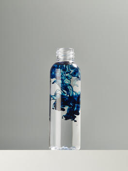 Blue color mixing with water in a clear bottle on a grey background.