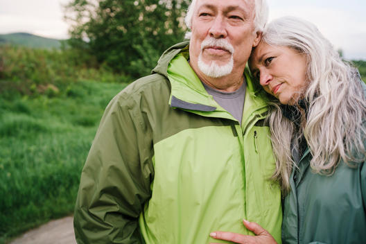 Portrait of a fit healthy older couple with grey silver hair standing on a dirt road and embracing.