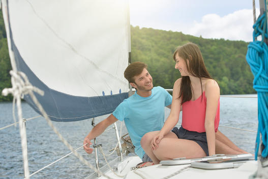 Young couple sailing on sunlit yacht over lake, smiling