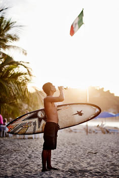 Surfer on a sun lit beach drinking beer
