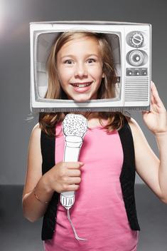 Girl speaking in microphone in paper TV against grey background