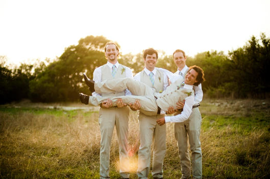 A groom is carried by his best men during a wedding day photo shoot in the Texas Hill Country.