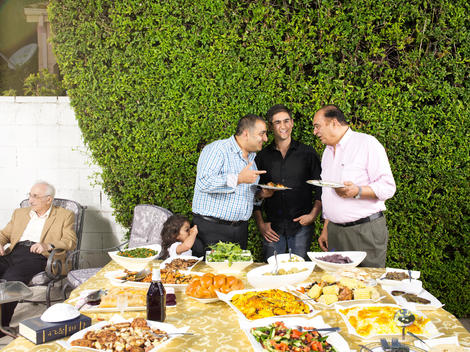 Alex Banayan stands at the end of a table covered in food in a backyard surrounded by his family members