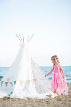 Young Girl in Fancy Dress Playing on Beach next to Teepee