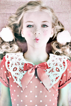 Female youth with pale skin wearing red spotted dress with bow, blonde hair in pig tails with makeup
