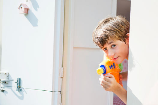 Boy holding water pistol and peering out of caravan, portrait
