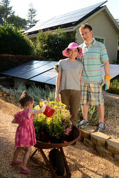 Young multiethic couple with their child enjoy green living and gardening in back yard with solar panels.
