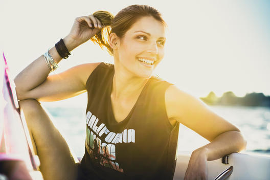 young woman wearing a fashionable outfit while sitting on a boat at summer, smiling and looking into the distance, back light and lens flare