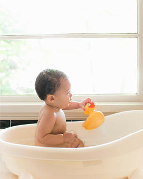 Baby girl sitting in bath holding rubber duck
