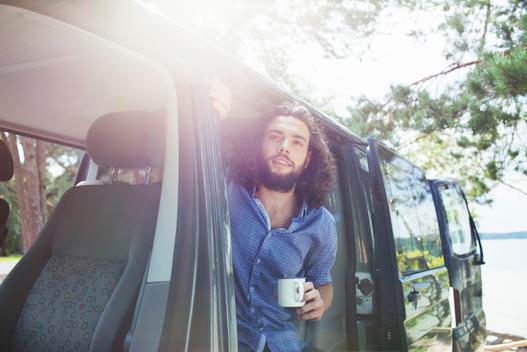Young man having coffee in van by lake