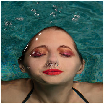 Beauty Image of a white woman?s face coming out water shot at high speed against a blue swimming pool