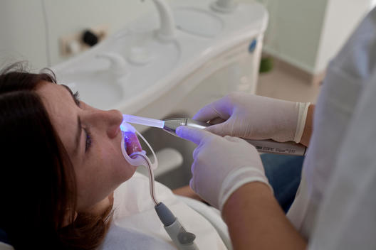 Dentist is working to dry her patients teeth with a blue laser stick to be able to get her patients teeth whitening.