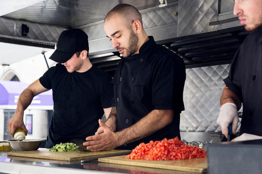 Cheerful group of chefs cutting vegetables inside food truck