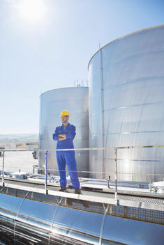 Worker with arms crossed on platform above stainless steel milk tanker