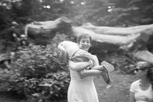 A smiling young mother playfully carries her son over her shoulder as she runs through the wood at the Donald and Barbara Zucker Natural Exploration for children at Prospect Park, Brooklyn, NYC