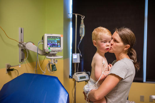 Grant, a young red-head boy, is held and kissed by his mother in the hospital, with tubes connected to his body, after nearly drowning in the pool before his mother pulled him out of the water. Heritage Hills, Colorado