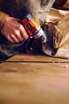 Cropped image of worker drilling nut into leather belt while manufacturing bag on workbench
