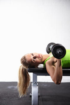 Young female athlete lying on bench training with bar bell in gym