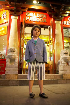 A well-dressed boy stands outside a Chinese restaurant.