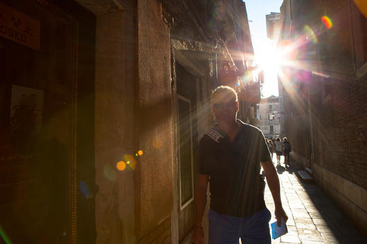 A man walking down a narrow street in Venice Italy as the sun comes down along the cobblestone area.