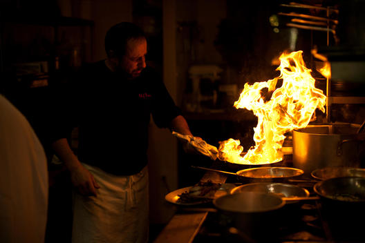 A chef works with a flaming pan on the stove.