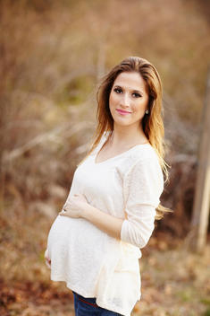 Pregnant woman holding her belly as she stands in a field in the afternoon.