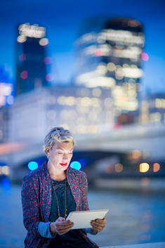 Mature businesswoman on Thames waterfront using digital tablet at night, London, UK