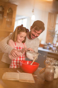 Father and daughter sifting flour into mixing bowl