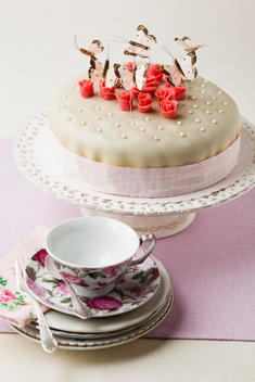 Cake decorated with butterflies shaped and marzipan, cup and saucer in foreground
